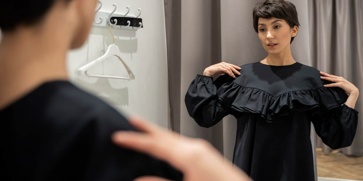 asian woman trying on a black dress in a dressing room with an unamused look on her face