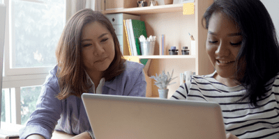 two asian women looking at a laptop and smiling