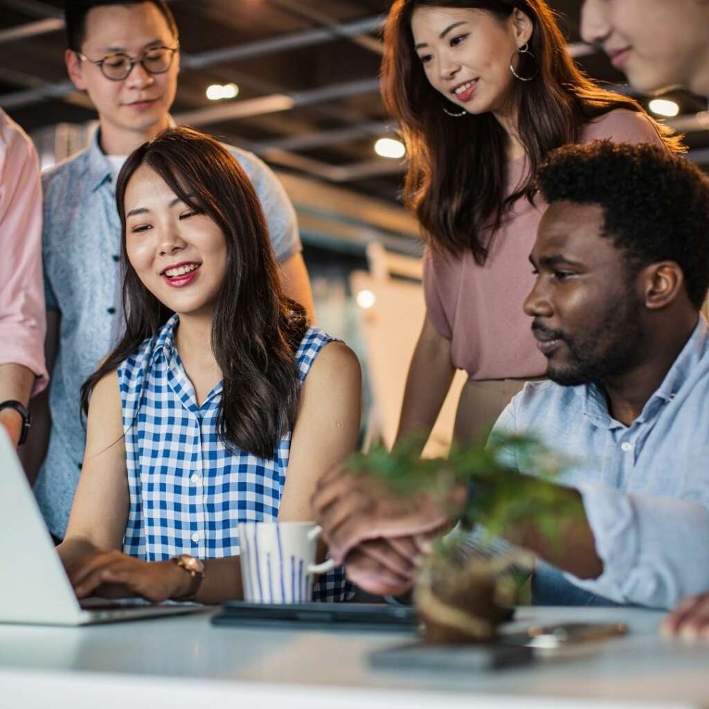 a group of millennials discussing something at a computer inside a well lit office space